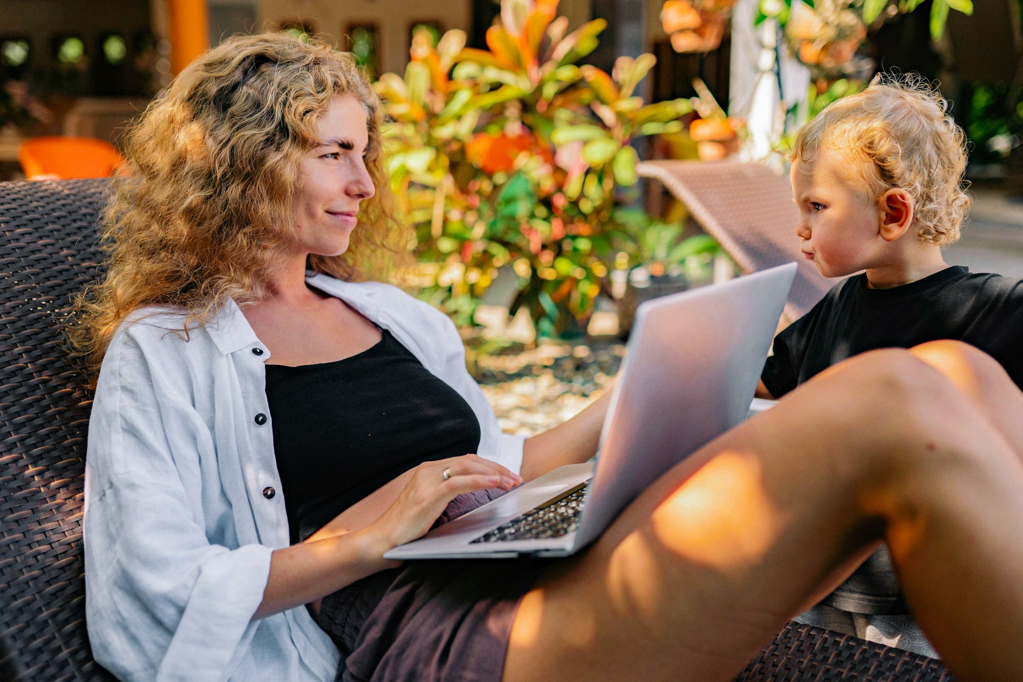 Mãe autônoma trabalhando ao ar livre com notebook ao lado do filho pequeno
