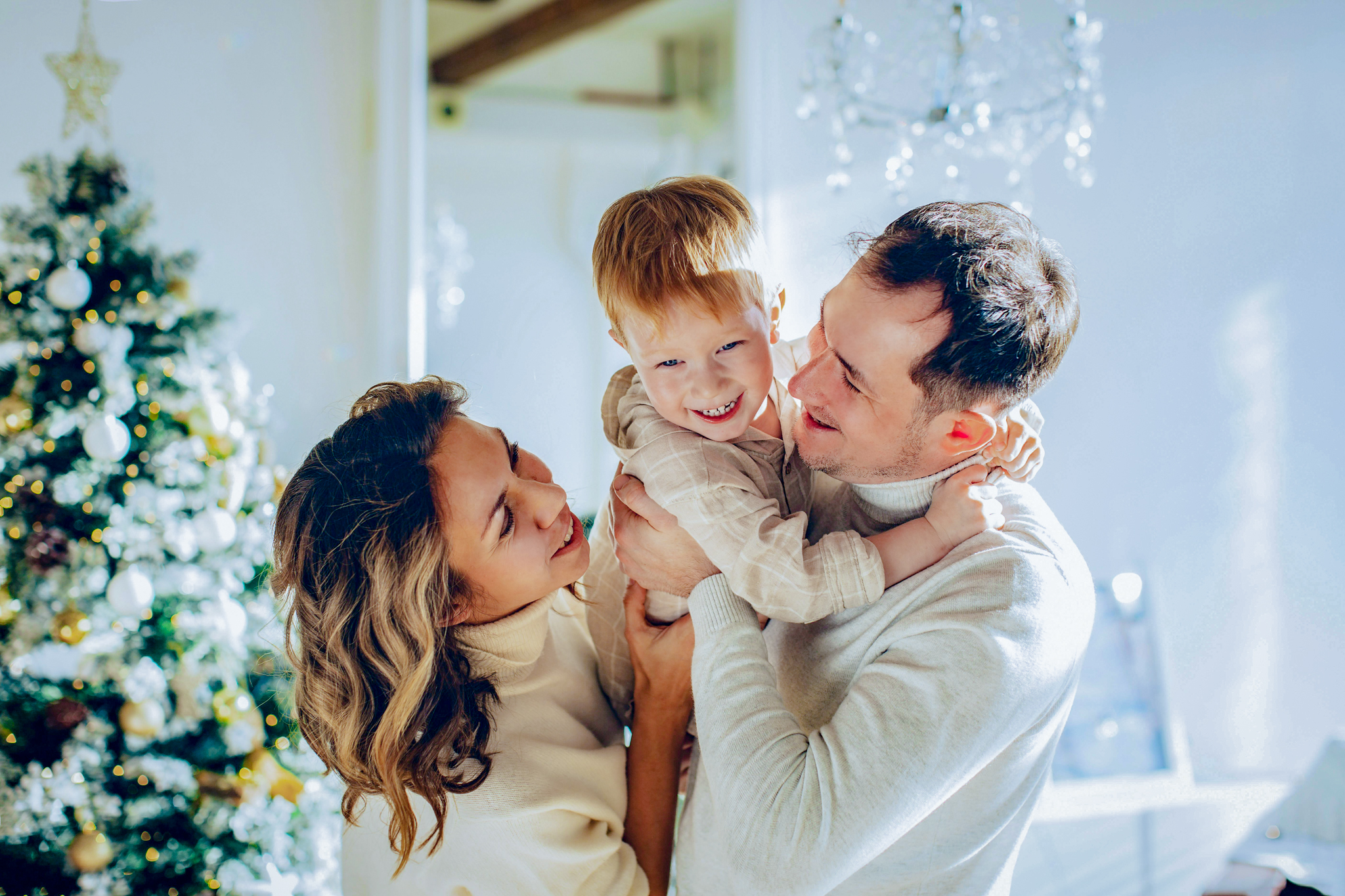 Família sorridente abraçando criança pequena em frente à árvore de Natal decorada